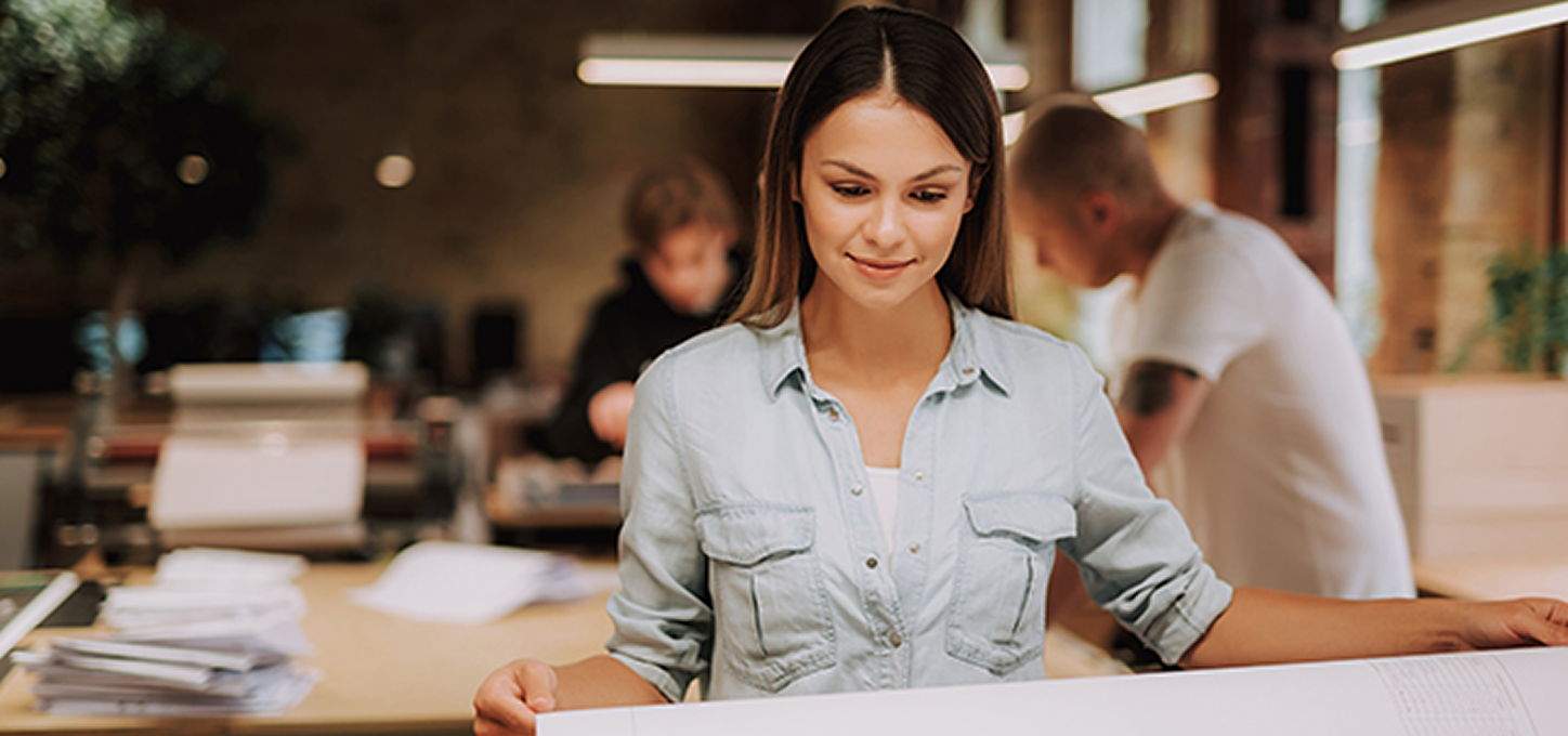 Moderne Produktionsumgebung mit einer Person, die ein großes Blatt präsentiert, um professionelle Druck‑Workflows darzustellen.